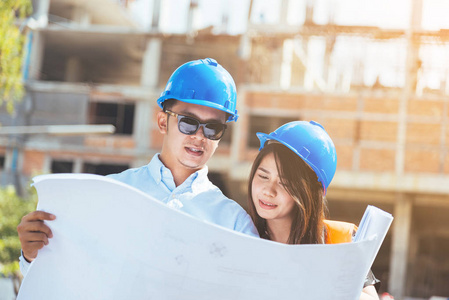 亞洲男女工程師與藍(lán)色安全頭盔會(huì)議在建筑工地與藍(lán)圖照片
